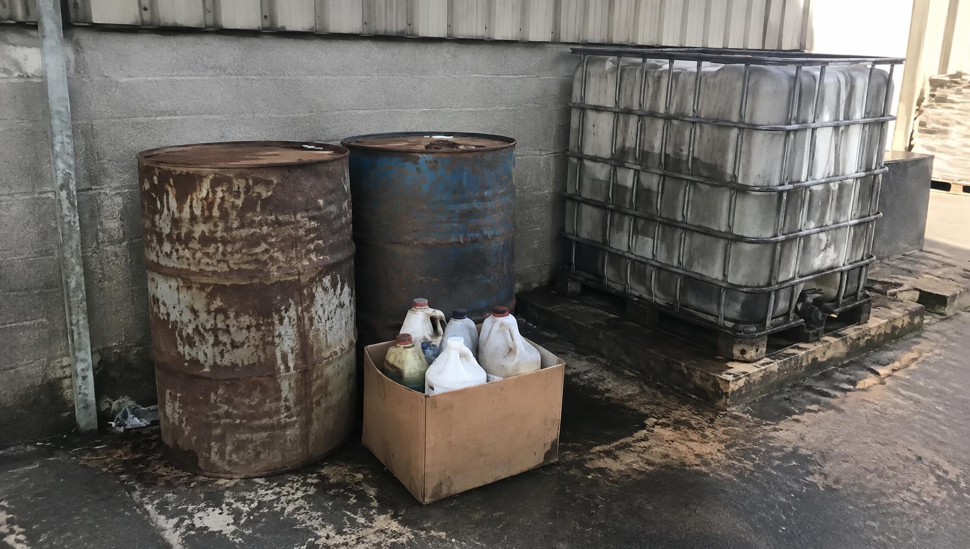 Labelled hazardous waste drums on a depot loading bay with a collection tanker